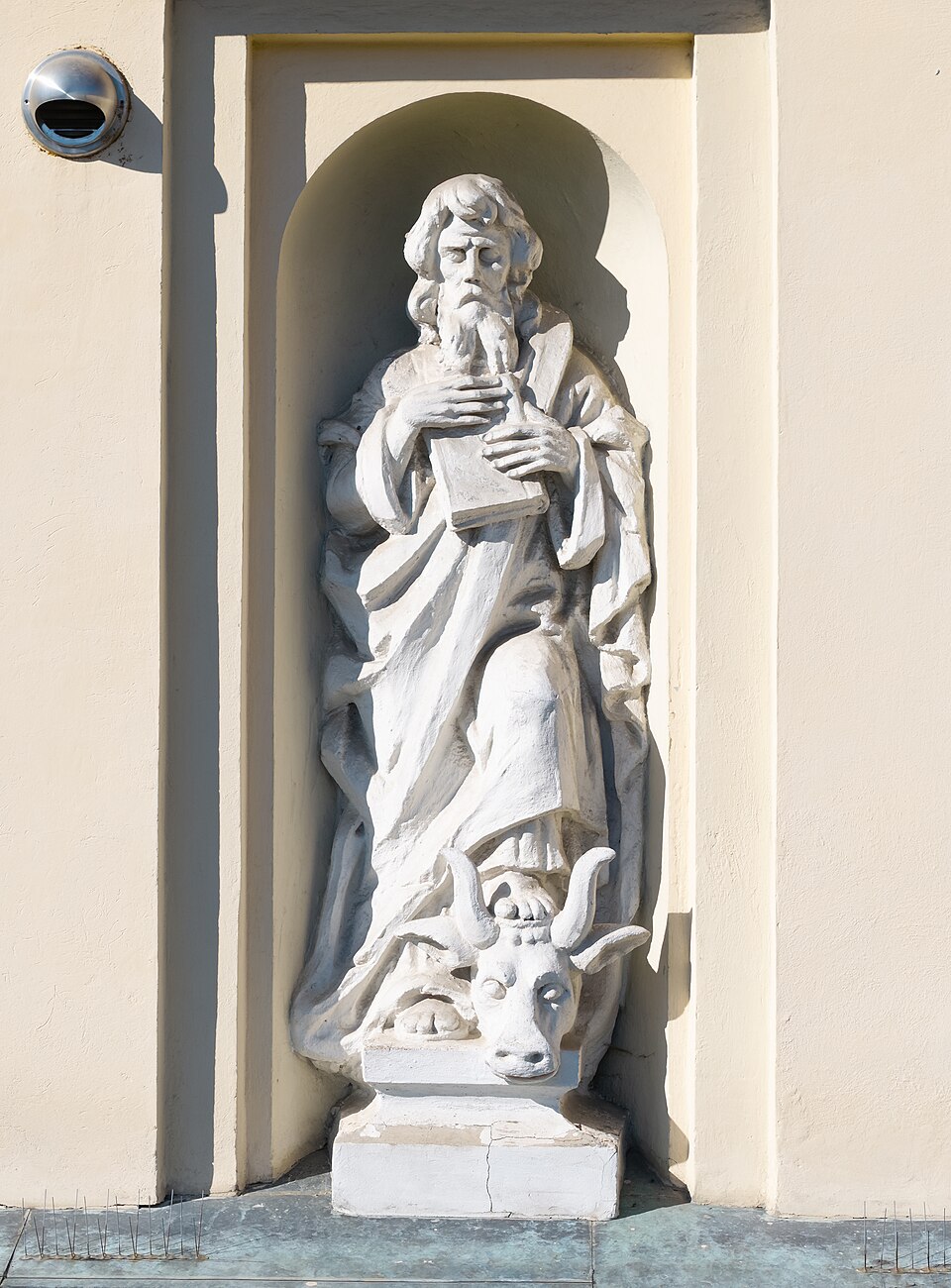 Estatua blanca de san Lucas en una hornacina, con barba, libro y pluma, y un toro a sus pies