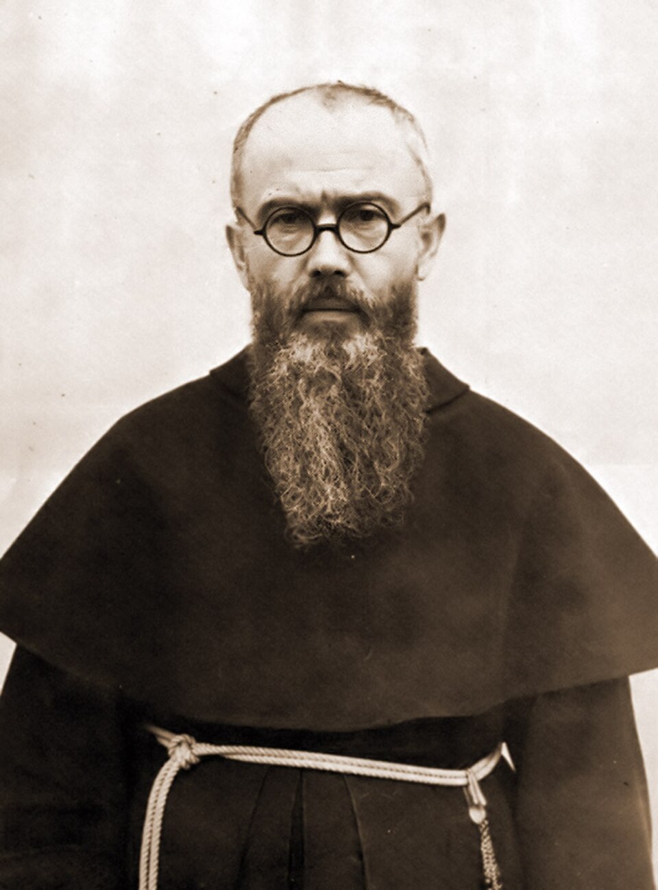 Fotografía en sepia de san Maximiliano María Kolbe con hábito franciscano, cordón, gafas redondas y larga barba