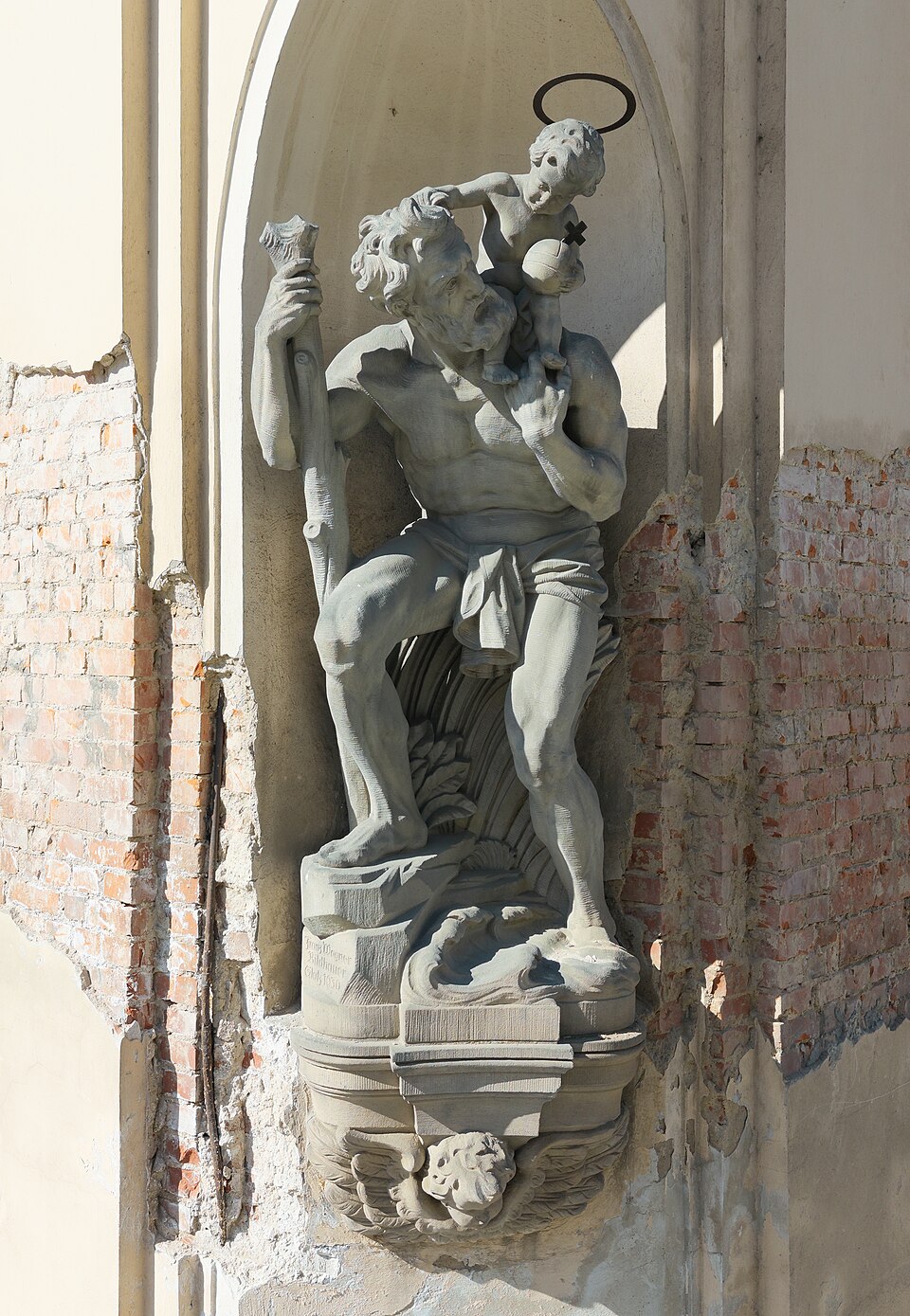 Escultura de piedra de san Cristóbal en una hornacina, con un bastón y el Niño Jesús sobre el hombro