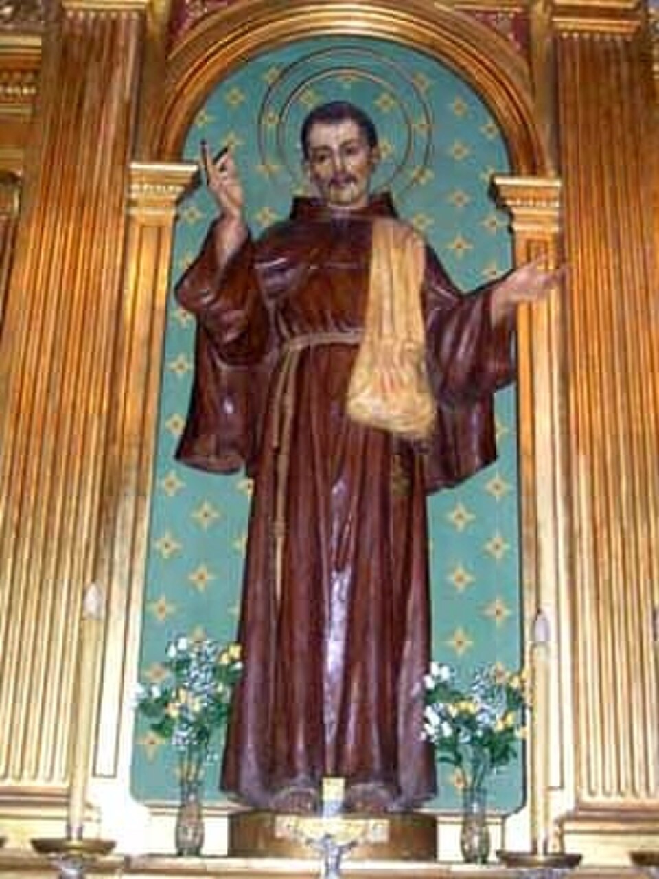 Talla del beato Buenaventura de Barcelona con hábito franciscano marrón, alforja al hombro y aureola, en un retablo dorado