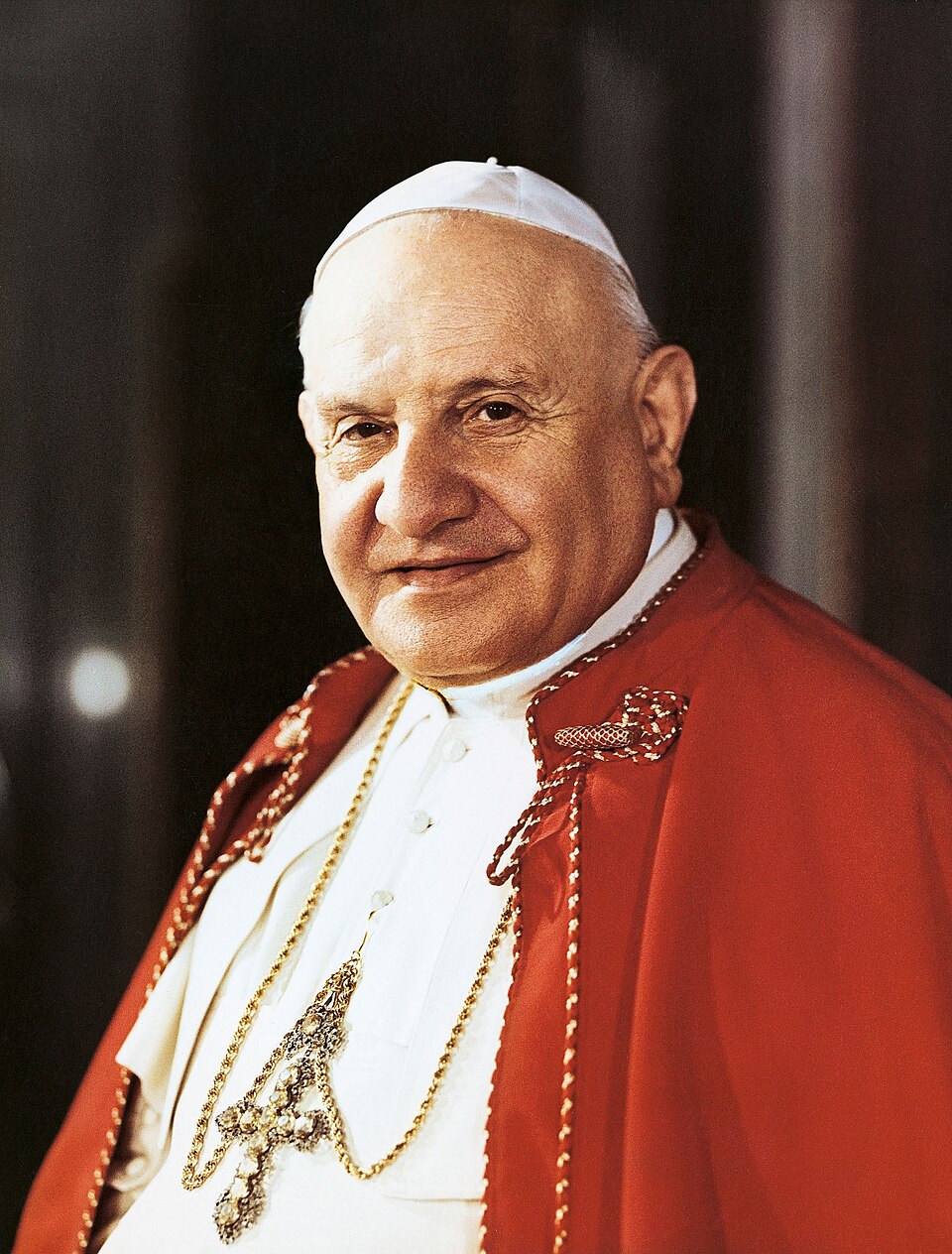 Fotografía en color de san Juan XXIII sonriente, con solideo blanco, muceta roja y cruz pectoral