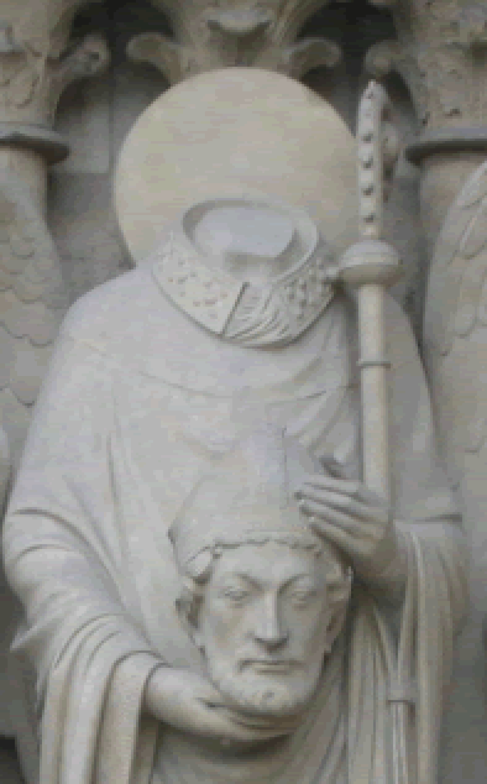 Escultura de piedra de san Dionisio con aureola y báculo, sosteniendo en sus manos su propia cabeza con mitra