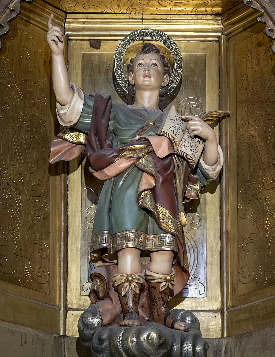 Escultura policromada de san Pancracio joven con aureola, señalando al cielo y sosteniendo un libro y una palma