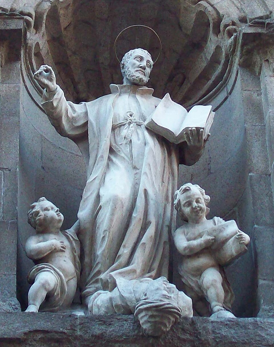 Escultura de piedra de san Cayetano con aureola, sosteniendo un libro abierto, flanqueado por dos angelotes