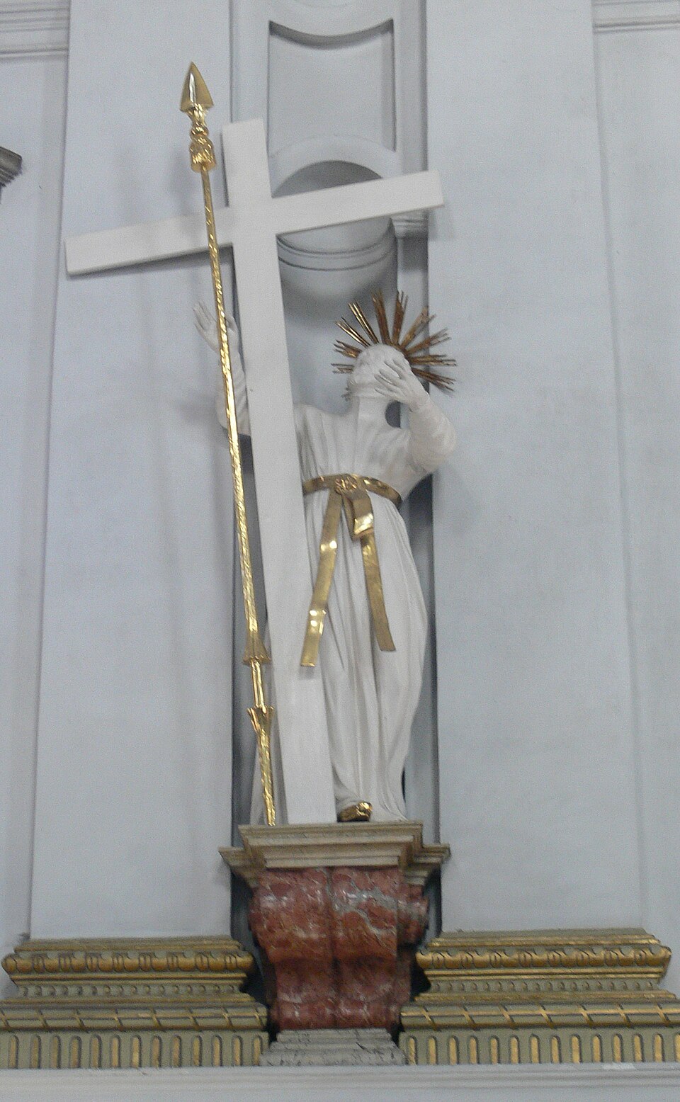 Estatua blanca de san Pablo Miki con resplandor dorado, tapándose el rostro junto a una gran cruz y una lanza