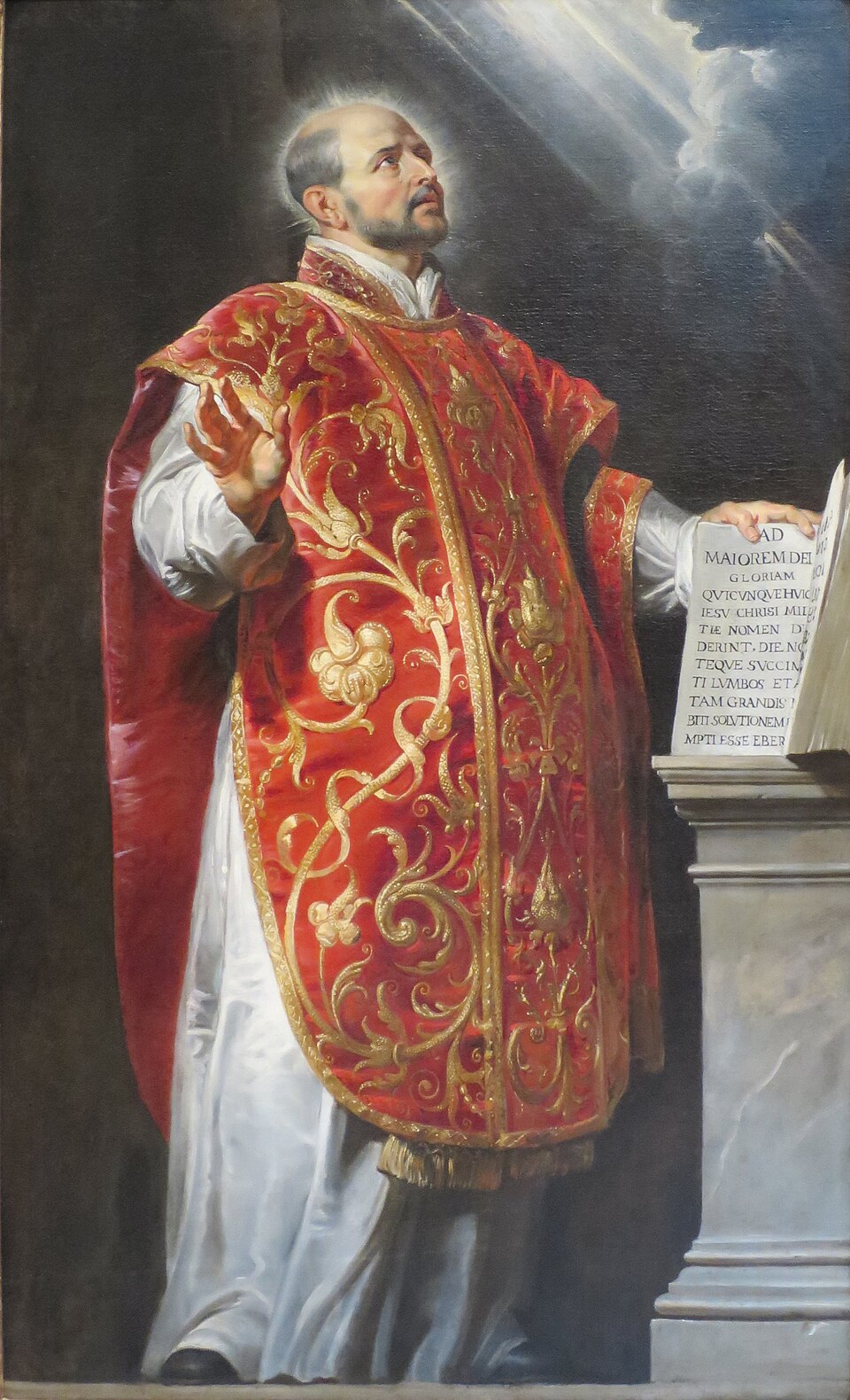 Pintura de san Ignacio de Loyola con casulla roja y dorada, mirando al cielo junto a un libro abierto