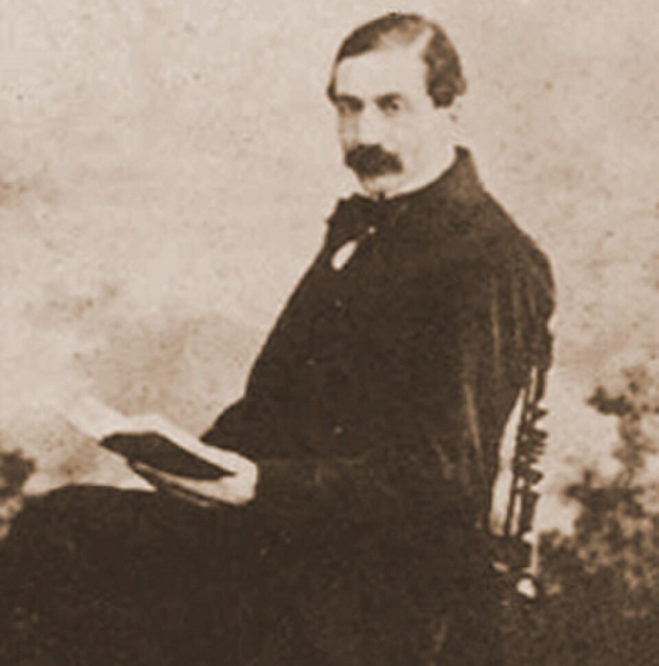 Fotografía antigua en sepia del beato Francisco Faà di Bruno sentado, con bigote y un libro abierto