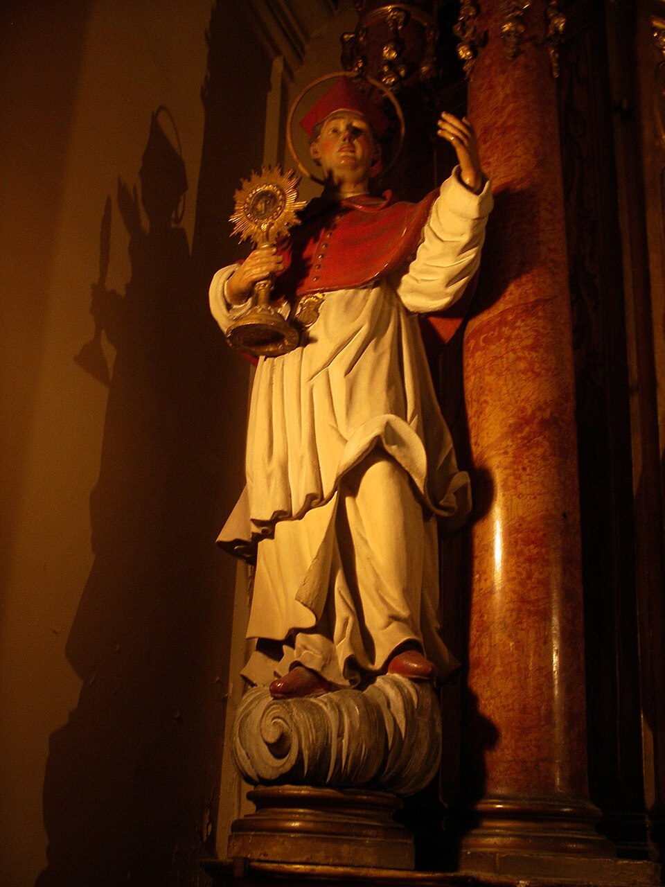 Escultura de san Ramón Nonato con birreta y muceta rojas y aureola, sosteniendo una custodia en la mano