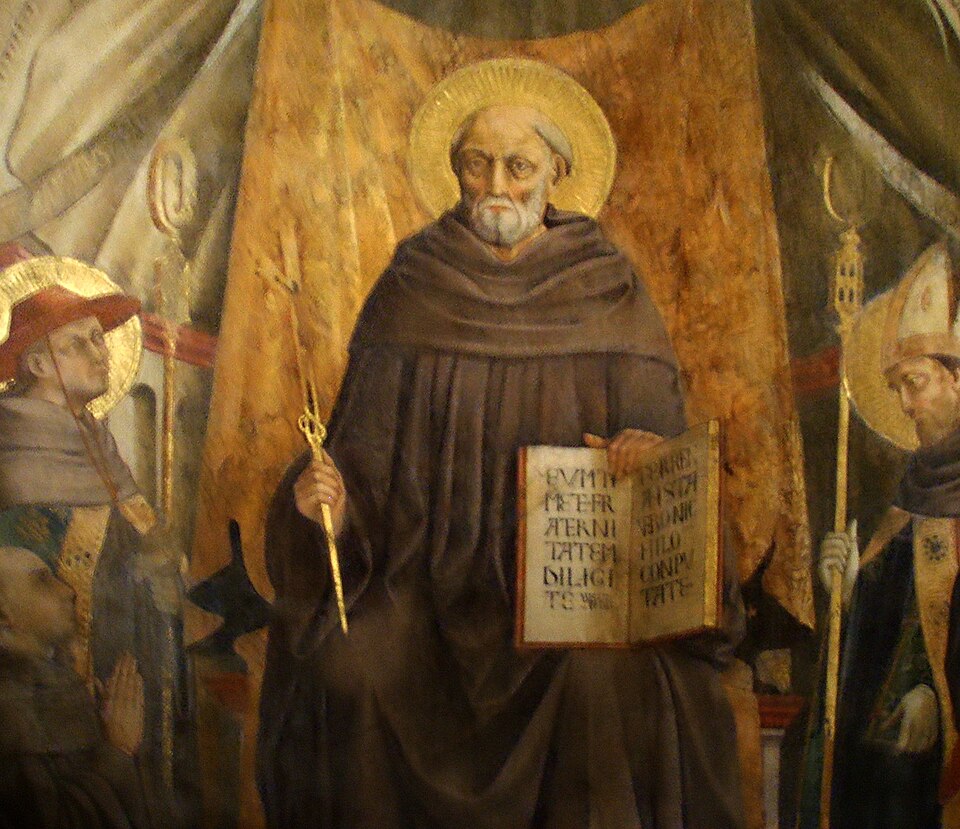 Pintura de san Juan Gualberto sentado, con hábito pardo y aureola, un bastón dorado y un libro abierto