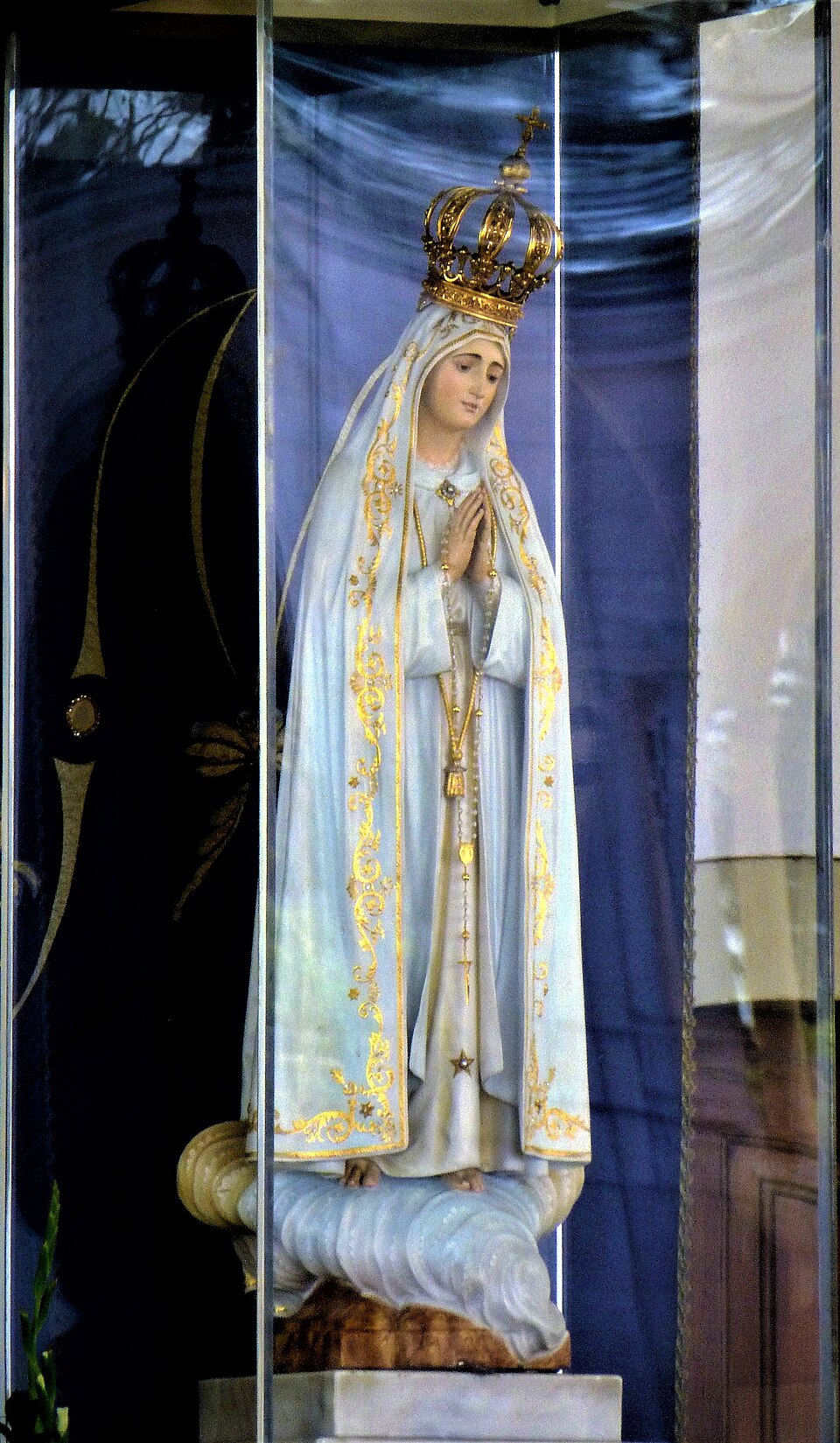 Imagen de Nuestra Señora de Fátima con manto blanco ribeteado en oro, corona y manos juntas con rosario